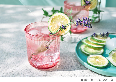 Cool lavender lemonade with lime slices and lavender flower on the table near pastel light blue background. Healthy organic summer soda drink. Detox water. Diet unalcolic coctail. Cool lavender lemonade with lime slices and lavender flower on the table near pastel light blue background. Healthy organic summer soda drink. Detox water. Diet unalcolic coctail. 96100118