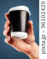 Male hand holds, raised black paper cup of tea or coffee. 96102420