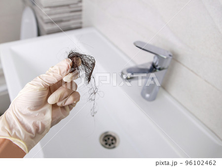 Lost hair in sink. A woman cleans the sink from garbage. Selective focus on the hand with hair. 96102462