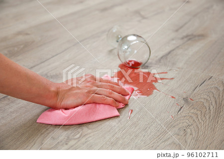 Glass of red wine fell on laminate, wine spilled on floor. A woman wipes the laminate from moisture. 96102711