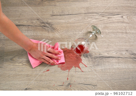 Glass of red wine fell on laminate, wine spilled on floor. A woman wipes the laminate from moisture. Glass of red wine fell on laminate, wine spilled on floor. A woman wipes the laminate from moisture. 96102712