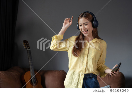 Happy woman listening music through wireless headphones standing on sofa at home. 96103049
