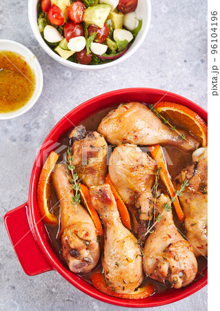 Chicken drumsticks with oranges and thyme baked in red round baking dish 96104196