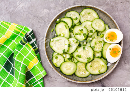 Ready-to-eat fresh cucumber salad, boiled chicken egg and green onions on a plate on the table. Top view 96105612