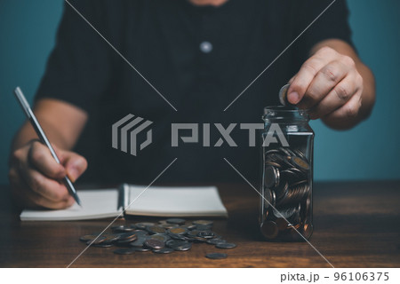 Young man putting coin in to jar and record amount of money in the notebook, saving, charity, family finance plan concept, fundraising, superannuation, investment, financial crisis concept.. 96106375