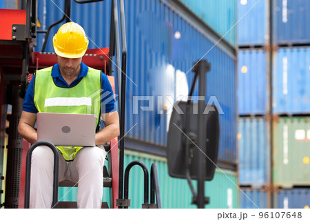 Young man working sitting on crane truck with computer at logistic import and export terminal industry.. 96107648