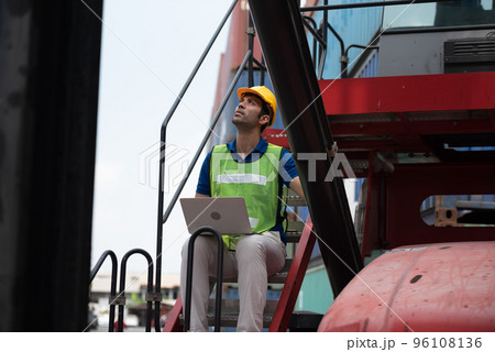Young man working sitting on crane truck with computer at logistic import and export terminal industry.. 96108136
