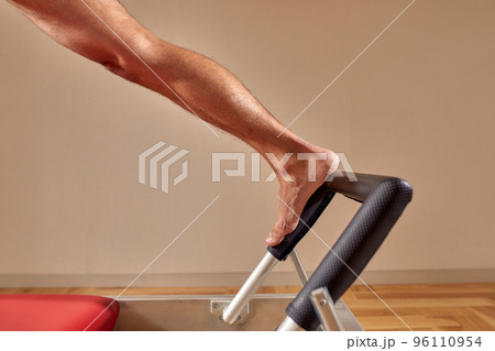 Side view of barefoot male athlete lying on pilates reformer and performing abs exercise during fitness workout. Pilates man concept. 96110954