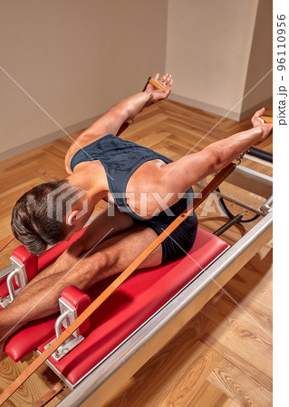 Fit man doing a lunge stretch yoga pilates exercise to strengthen and tone his muscles using a reformer in a gym 96110956