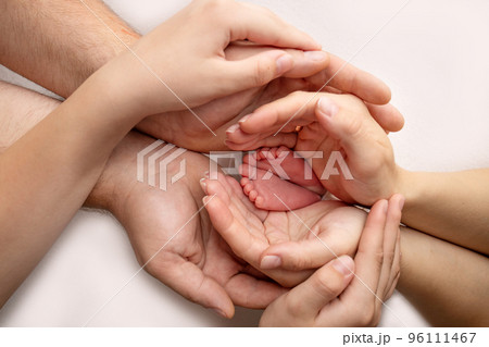 Baby feet in the hands of mother, father, older brother or sister, family. Feet of a tiny newborn close up. Little children's feet surrounded by the palms of the family. Parents and their child. Baby feet in the hands of mother, father, older brother or sister, family. Feet of a tiny newborn close up. Little children's feet surrounded by the palms of the family. Parents and their child. 96111467
