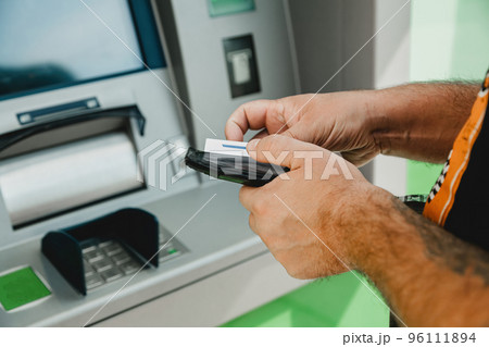 Man ATM card. ATM insert card. Man putting credit card in atm machine while holding wallet Man ATM card. ATM insert card. Man putting credit card in atm machine while holding wallet 96111894