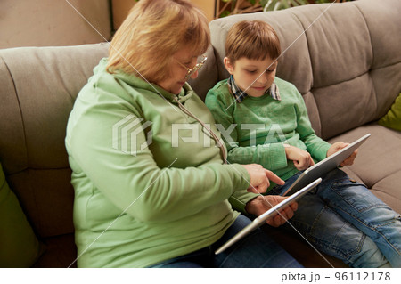 Middle age woman and school age boy, granny and grandson sitting at home and talking, having fun. Concept of emotions, family, happiness, care, support and leisure activities Middle age woman and school age boy, granny and grandson sitting at home and talking, having fun. Concept of emotions, family, happiness, care, support and leisure activities 96112178