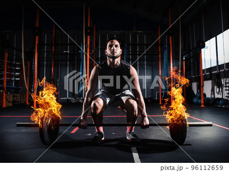 Athletic man works out at the gym with a fiery barbell 96112659
