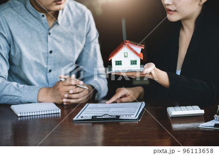 Concept of signing loan agreements, refinancing, buying and selling houses and land, focusing on model houses. A real estate agent is pointing to contract documents for male clients to Buy a dwelling Concept of signing loan agreements, refinancing, buying and selling houses and land, focusing on model houses. A real estate agent is pointing to contract documents for male clients to Buy a dwelling 96113658