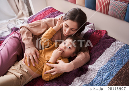 Woman laying at the bed and embracing with her son with Down syndrome 96113907