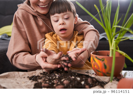 Boy with down syndrome holding ground at his hands while helping to his mother replacing flowers 96114151