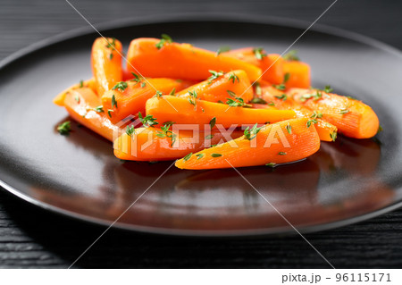Baked (roasted) honey glazed baby carrots with thyme on a dark ceramic plate, close-up. Baked (roasted) honey glazed baby carrots with thyme on a dark ceramic plate, close-up. 96115171