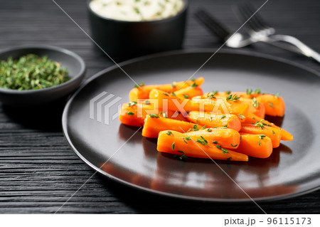 Baked (roasted) honey glazed baby carrots with thyme with yogurt creamy sauce on ceramic plate on a dark wooden table. Baked (roasted) honey glazed baby carrots with thyme with yogurt creamy sauce on ceramic plate on a dark wooden table. 96115173