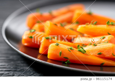 Baked (roasted) honey glazed baby carrots with thyme on a dark ceramic plate, macro shot. Baked (roasted) honey glazed baby carrots with thyme on a dark ceramic plate, macro shot. 96115174