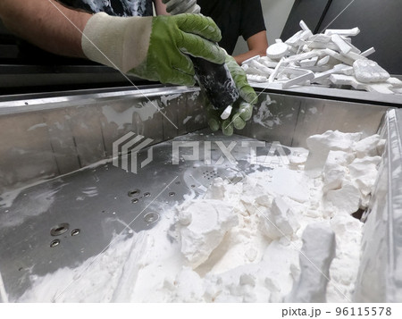 A man working with a working vacuum cleaner to clean the white powder of polyamide from a model printed on a 3D printer inside a 3D printer. Cleaning objects printed on an industrial powder 3D printer 96115578