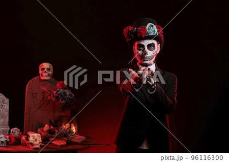 Woman dressed as catrina skull to celebrate dios de los muertos in studio, reaching with hand to lure and tempt. Creepy goddess of death with mexican holiday costume, traditional body art. Woman dressed as catrina skull to celebrate dios de los muertos in studio, reaching with hand to lure and tempt. Creepy goddess of death with mexican holiday costume, traditional body art. 96116300