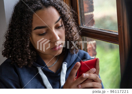Sad Biracial African American Teenager Woman Using Cell Phone for Social Media 96117221