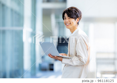 オフィスのロビーでノートパソコンを持って立っている若い男性 96118125