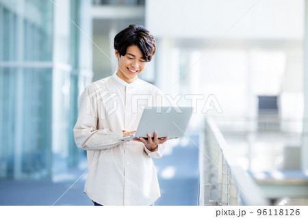 オフィスのロビーでノートパソコンを持って立っている若い男性 96118126