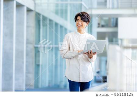 オフィスのロビーでノートパソコンを持って立っている若い男性 96118128