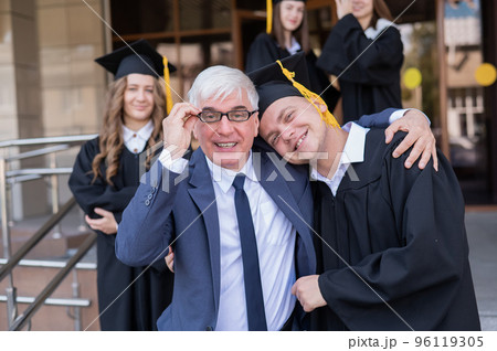Father and son embrace at graduation. Parent congratulates university graduate. Father and son embrace at graduation. Parent congratulates university graduate. 96119305