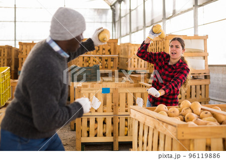 Man and young woman vegetable storehouse workers throwing pumpkins at each other 96119886