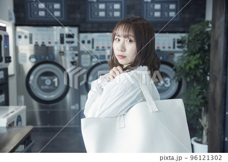 コインランドリーでランドリーバッグを持つ若い女性 96121302
