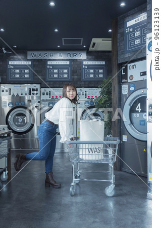 コインランドリーでランドリーカートを押す若い女性 96123139
