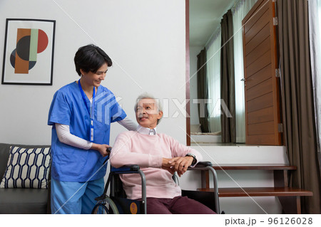 Friendly staff caregiver of nursing home talking to asian senior man in living room 96126028