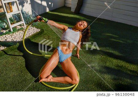 Young woman refreshing herself with garden hose 96130048