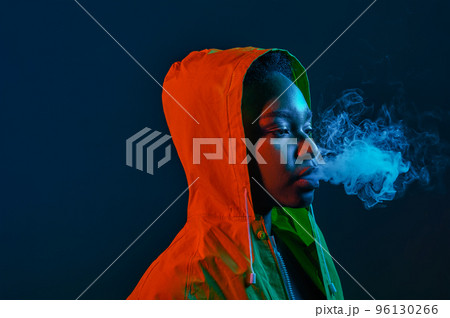 Hipster woman in raincoat blowing smoke from mouth Hipster woman in raincoat blowing smoke from mouth 96130266