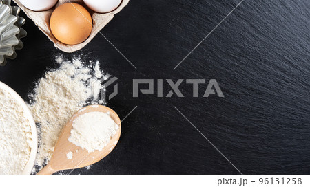Baking ingredients flour, eggs, milk, bakeware on black slate background with copy space 96131258
