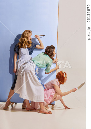 Portrait of three beautiful women peeking out corner with knives isolated over grey background. Revenge Portrait of three beautiful women peeking out corner with knives isolated over grey background. Revenge 96133679