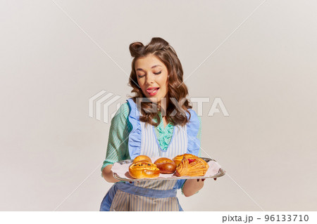 Portrait of stylish young woman, housewife with freshly baked buns isolated over grey background 96133710