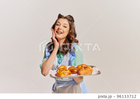 Portrait of elegant young woman, housewife with freshly baked buns isolated over grey background 96133712
