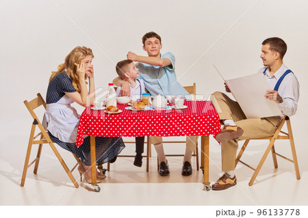 Portrait of lovely young family, woman, man and two boys sitting at the table and having breakfast isolated over grey background 96133778