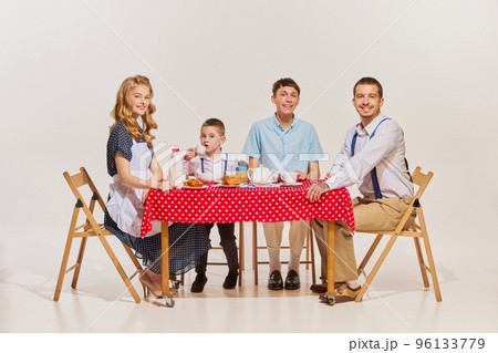 Portrait of lovely young family, woman, man and two boys sitting at the table and having breakfast isolated over grey background 96133779