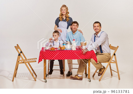 Portrait of lovely young family, woman, man and two boys sitting at the table and having breakfast isolated over grey background 96133781