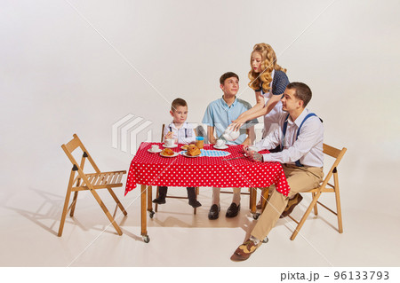Portrait of young happy family sitting at table together and having breakfast isolated on grey background 96133793