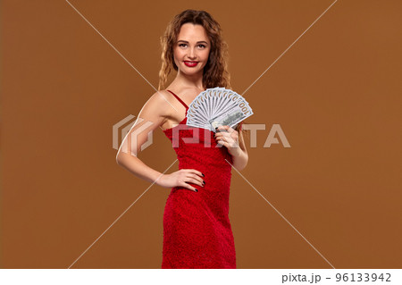 Blond curly woman weared in a red sexy dress is holding some hundred dollar bills in her hands. Casino. Blond curly woman weared in a red sexy dress is holding some hundred dollar bills in her hands. Casino. 96133942