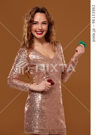 Blond woman weared in a gold glittered dress is holding some colorful gambling chips in her hands. Casino. Blond woman weared in a gold glittered dress is holding some colorful gambling chips in her hands. Casino. 96133962