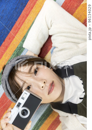 ラグマットに寝転んでフィルムカメラで写真を撮る若い女性 96134029