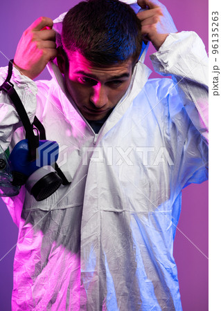 Coronavirus covid-19 pandemic. Doctor scientist wearing protective biological suit and mask due to global healthcare epidemic warning and danger background in blue and pink neon lights background. 96135263