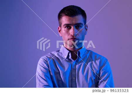 A man in a shirt poses on a dark multicolored neon background A man in a shirt poses on a dark multicolored neon background 96135323