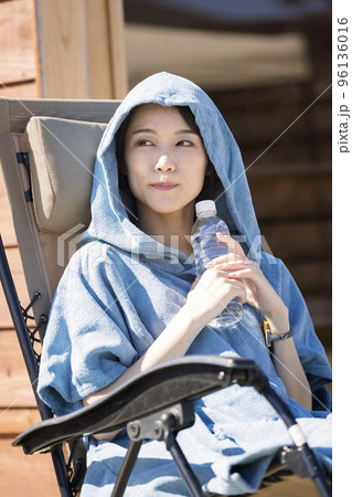 屋外サウナの前でサウナポンチョを着て外気浴をするサウナ女子 96136016